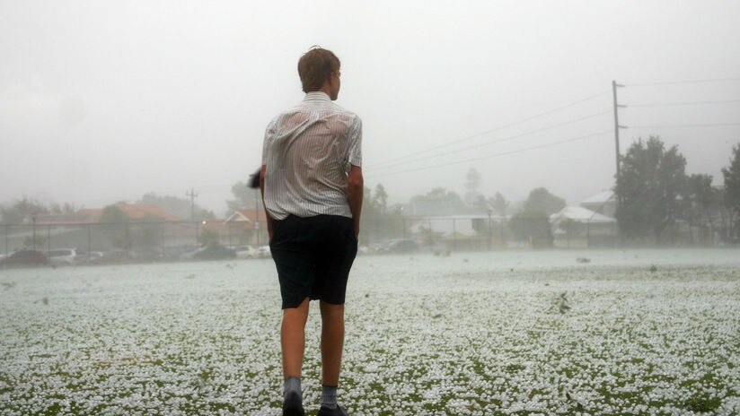 A boy stands in the middle of a playing field covered in hailstones.