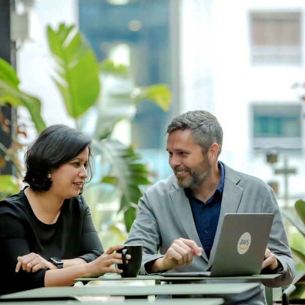 A man is pointing at a laptop while talking to a woman