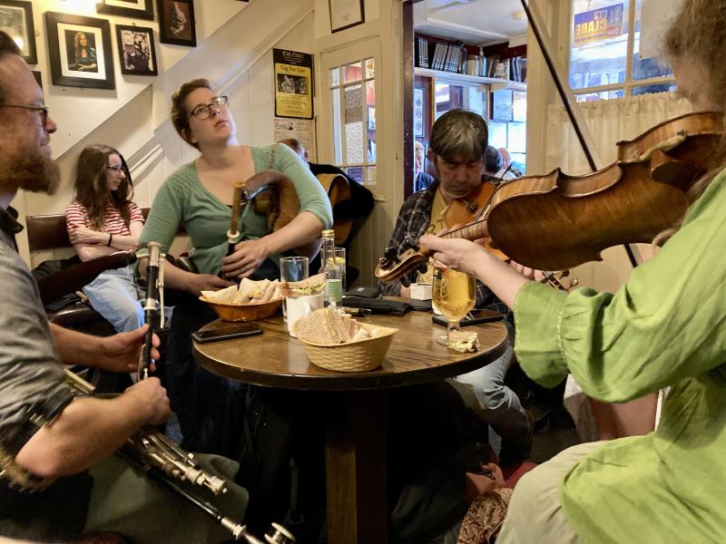 Pipers and fiddlers playing around a table in a pub.