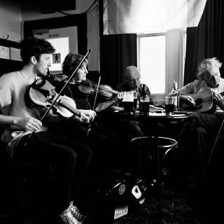 Two fiddlers, a whistler and a guitarist playing around a pub table.