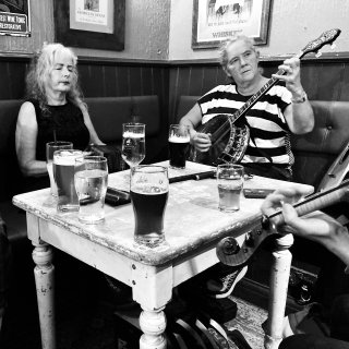 A concertina player, banjo player, and fiddler playing round a pub table festooned with pints.