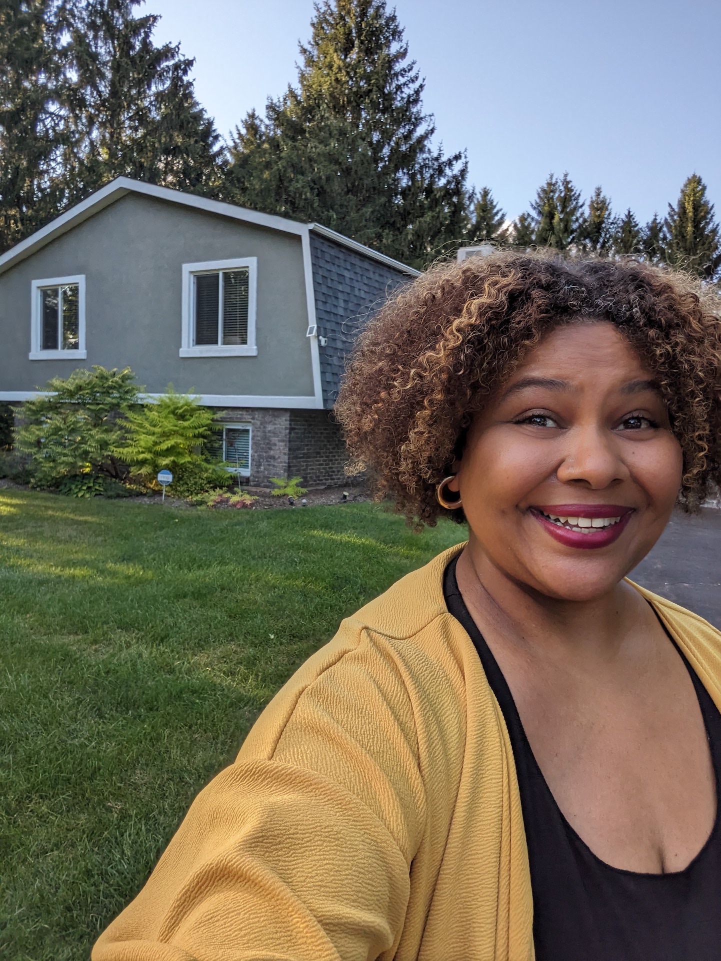 Afrobella smiling in front of a house she saw on a real estate visit