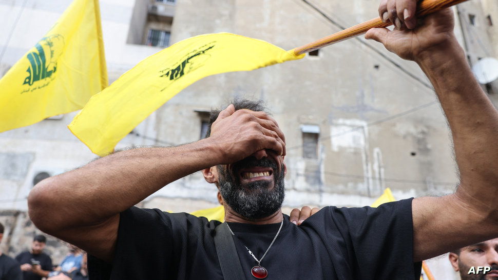 A man reacts while holding a Hezbollah flag during the funeral of people killed after hundreds of paging devices exploded in a…