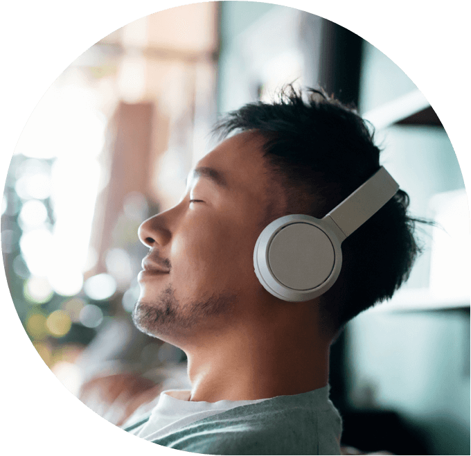 A smiling Asian man relaxes while listening to music on white headphones.