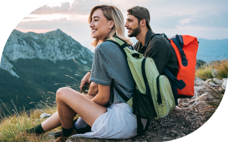 A backpacking couple sit on a mountaintop, smiling and taking in the view.