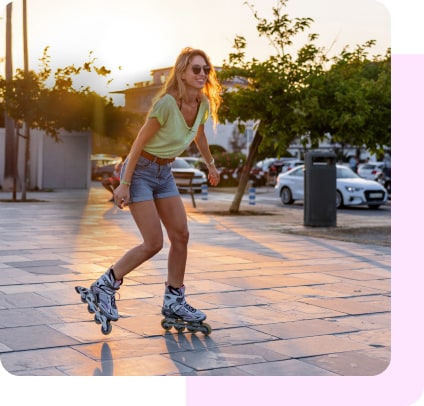 A woman in summer clothing and sunglasses rollerblades outside at sunset.