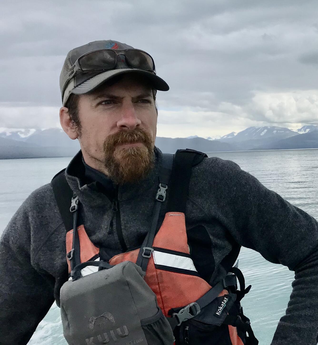 Portrait of a man wearing outdoor gear with a lake and distant mountains in the background