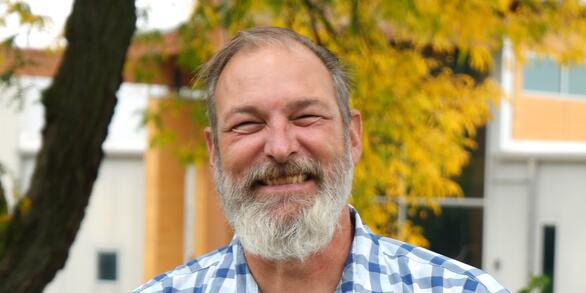 Smiling man with white beard standing in front of autumn tree