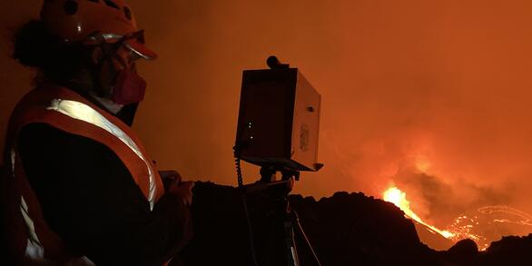 person in protective gear using a spectrometer on the rim of Halema‘uma‘u crater