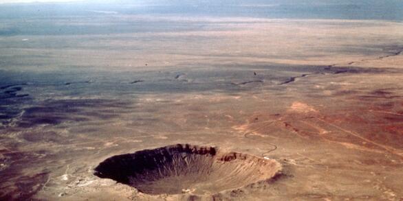 Aerial photograph showing a large, deep, circular depression with an elevated rim in the barren desert