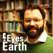 Mugshot of bearded man with bookshelves behind him and a little white text 