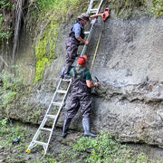 two people measuring a rock outcrop, one is on a ladder