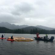 Scientists in two kayaks and a motorboat setting up round floating limnocorrals on McKinley Lake, Alaska.