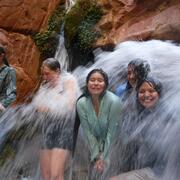 Partners in Science trip participants cool down under a small waterfall on a hot day