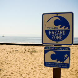 A sign at a beach warns that it's a tsunami hazard zone and that in case of earthquake to go to high ground or inland.