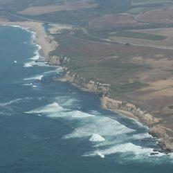 Aerial view of coastal bluffs, marine terrace with farmland, beach in distance with lagoon, highway runs along coast.