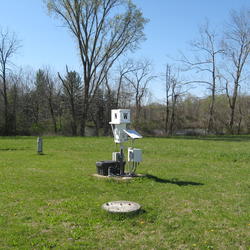 NADP Raingage in an open field; trees and a lake visible in the background