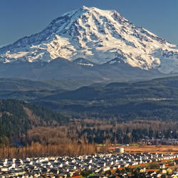 Large snow-covered, cone shaped mountain in background, looming over urban area in foreground