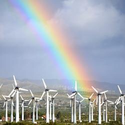 Tall wind turbines in a semi-arid shrubland with a bright rainbow