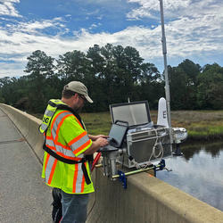 USGS technician on a bridge with instruments and laptop