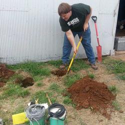 person digging a hole next to a building with seismometers nearby on the ground