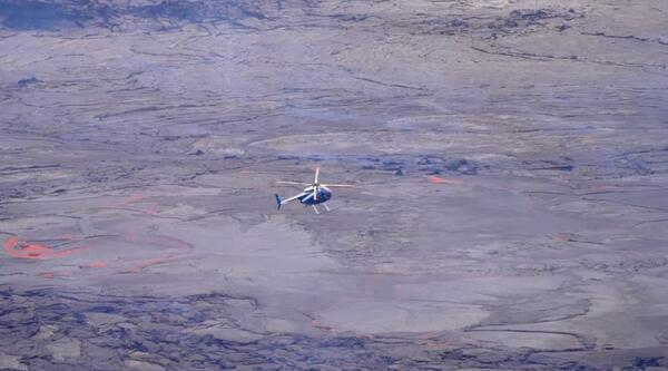 Color photograph of helicopter with lava in background