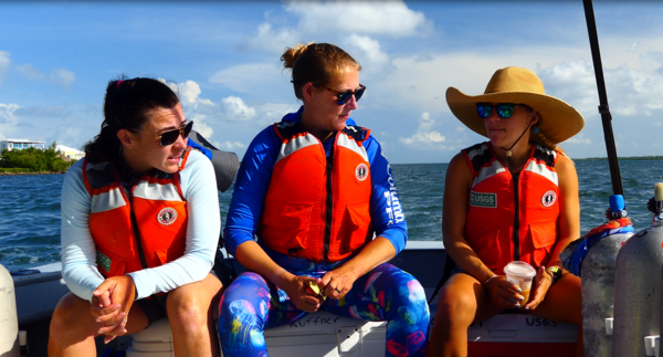 Three USGS scientists sit on the back of a research vessel and prepare for a dive.