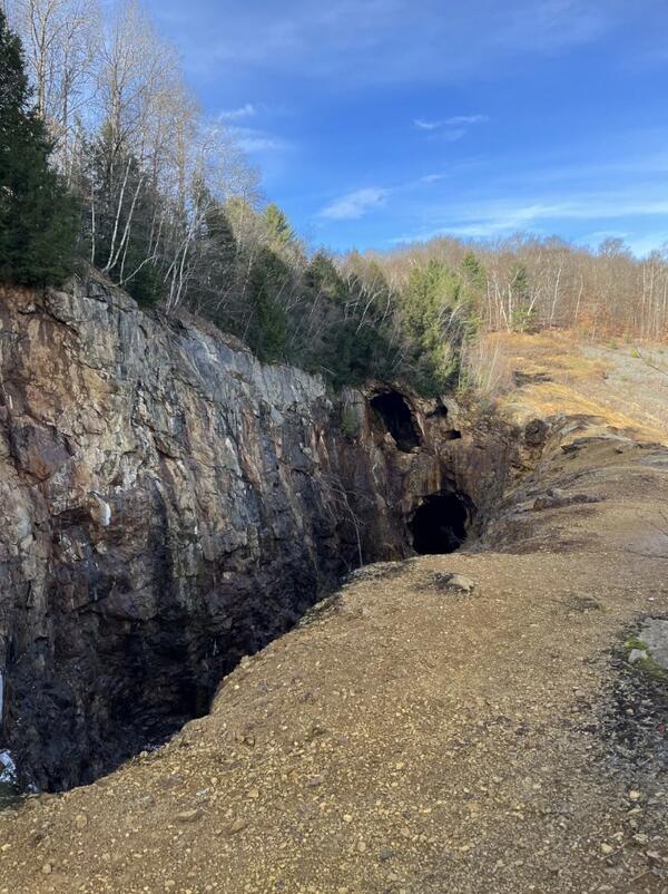 Abandoned mine tunnels in bedrock with trees on the left-hand side.