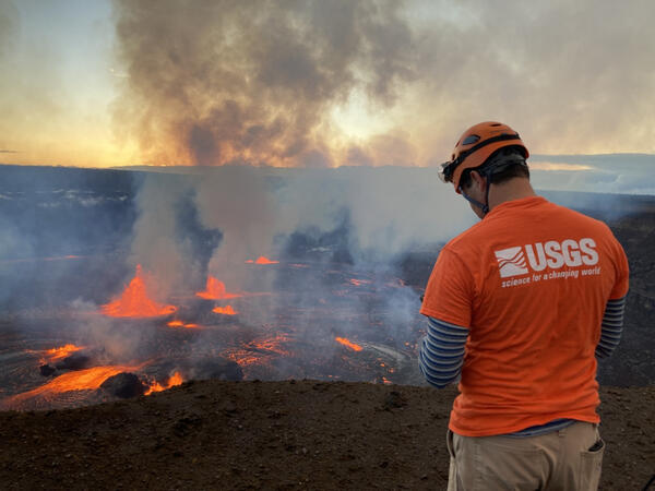 scientist wearing a helmet stands facing Halemaʻumaʻu crater