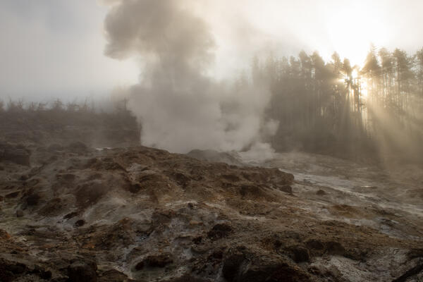 steam rising from a rocky hill with the sunrise breaking through the trees on the side.