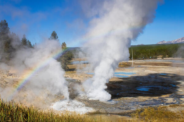 A rainbow rises to the right over the fumes of two geysers nearby.