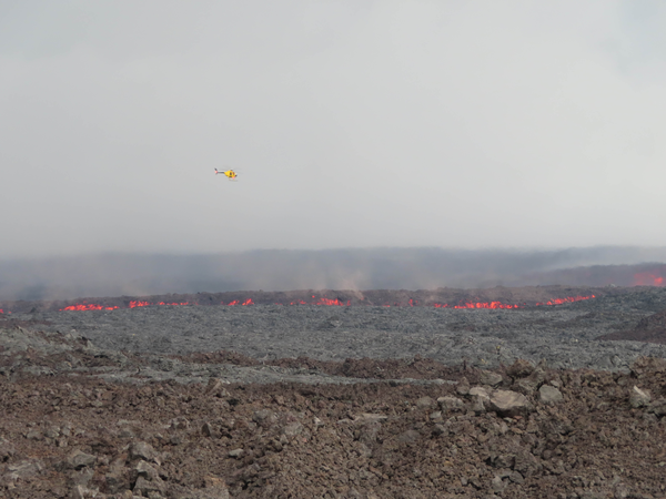 A helicopter flies over the lava flow