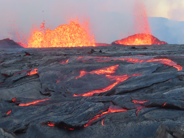 lava fountains at the summit of Kīlauea with black and glowing lava in the foreground