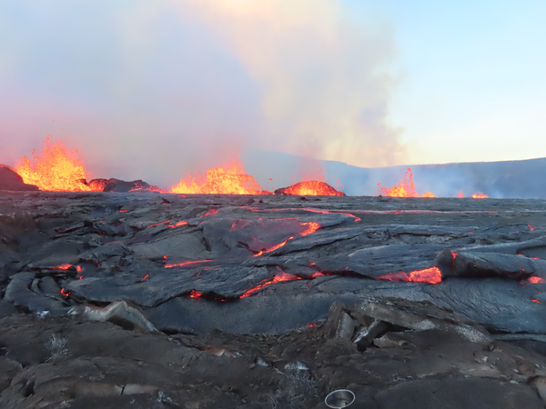 lava fountains at the summit of Kīlauea with black and glowing lava in the foreground