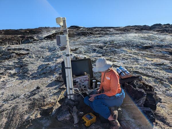 Color photograph of scientist conducting maintenance on volcanic gas monitoring station