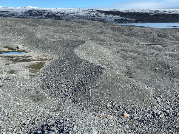 a curvy ridge of loose rocks and gravel sit in the foreground with a glacier in the background