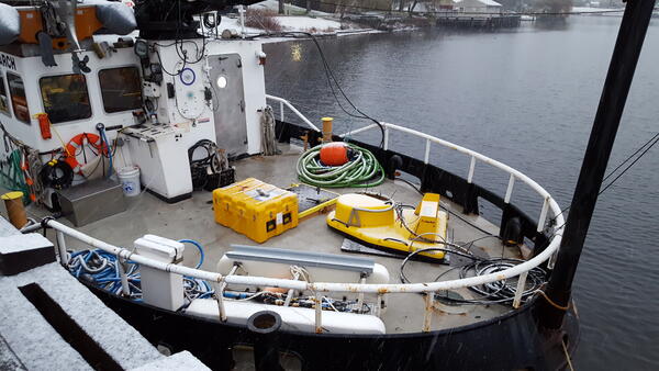 Photo of equipment sitting on the deck of a boat which is docked, and it's sleeting or snowing.