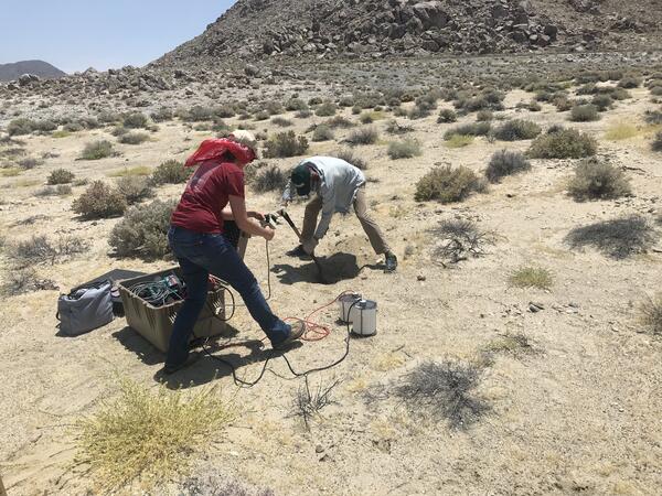 two people working with instruments in an arid area