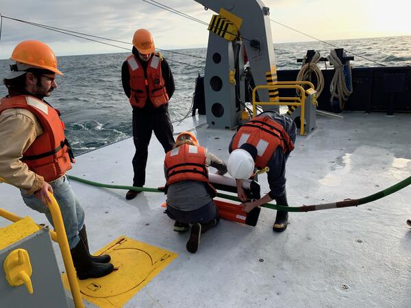 People on the deck of a research vessel handling a piece of scientific equipment