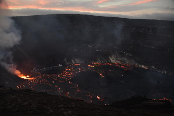 Low-light photograph of a lava lake with bright lava fountains erupting from the vent in the west crater wall