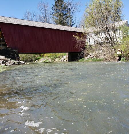 Photograph of technician measuring streamflow in a stream with a covered bridge