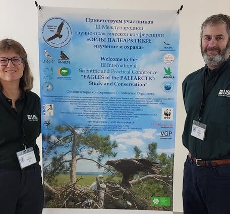 two people standing on either side of a conference poster, the poster has a picture of an adult eagle and its chick in a nest