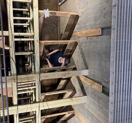 Young man wearing a hard hat stands in the wooden baffles of a de-watered fish ladder