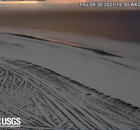 Photo looks down to a coastal area with ice and snow and the open ocean in the background.