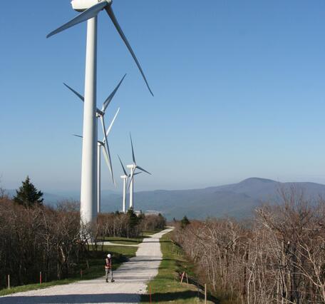 person on a gravel road along side a row of wind turbines