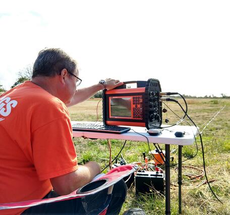 man in fields in chair reading data from instrument on table