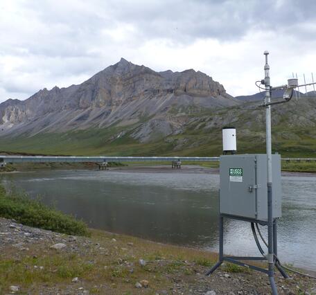 A streamgage with the Alyeska pipeline in the background