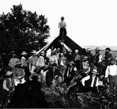 Thirty men posed around a canvas tent