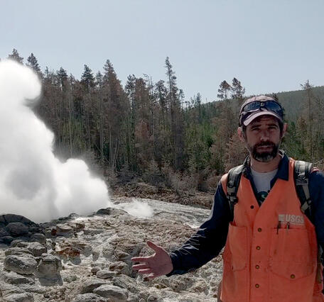 Man standing in front of a geyser with orange vest on