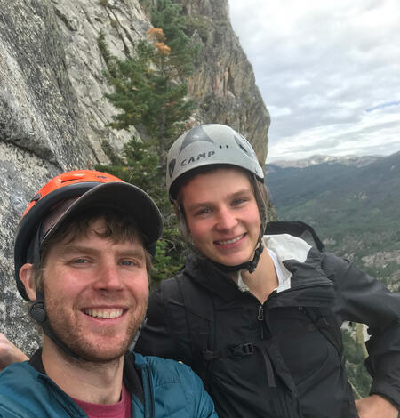 two people with climbing helmets next to vertical rock face